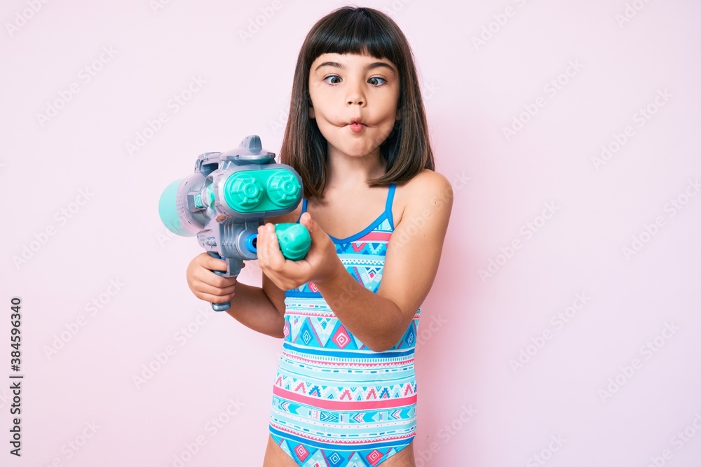 Young little girl with bang wearing swimsuit and watergun making fish face with mouth and squinting eyes, crazy and comical. Young little girl with bang wearing swimsuit and watergun making fish face with mouth and squinting eyes, crazy and comical.