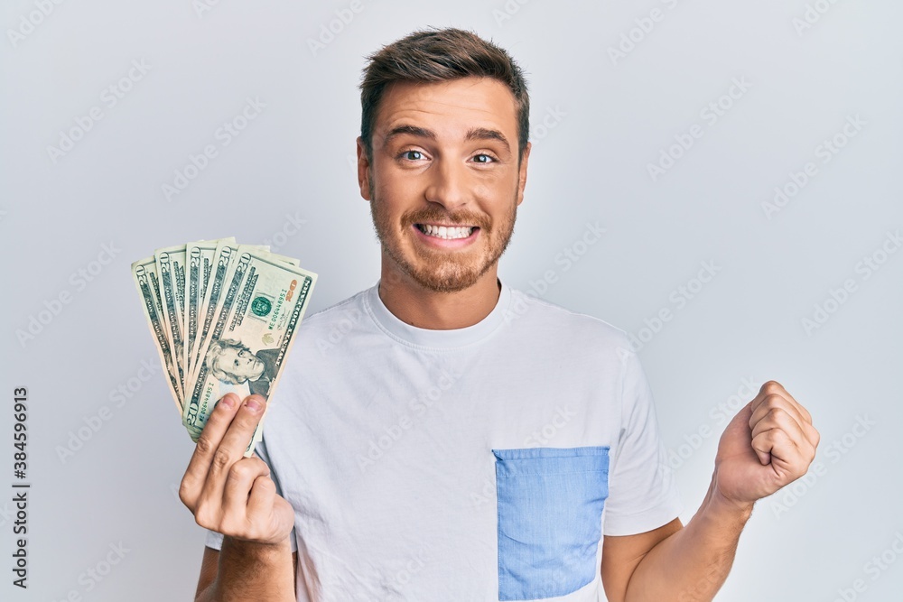Handsome caucasian man holding 20 dollars banknote screaming proud, celebrating victory and success very excited with raised arm Handsome caucasian man holding 20 dollars banknote screaming proud, celebrating victory and success very excited with raised arm