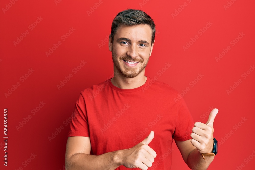 Handsome caucasian man wearing casual red tshirt pointing to the back behind with hand and thumbs up, smiling confident