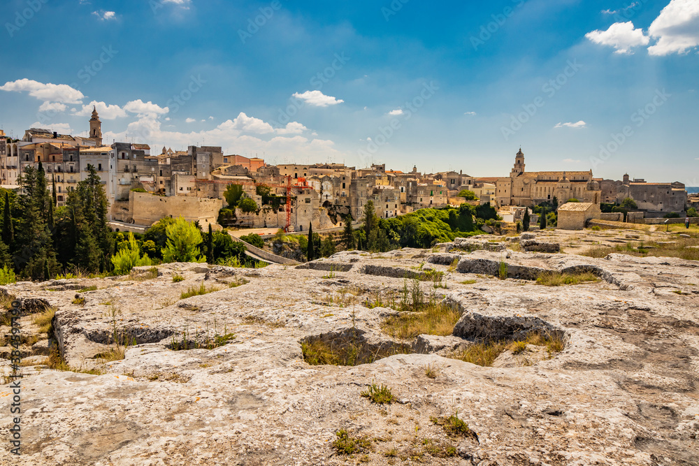 Gravina in Puglia, Italy. The archaeological park of Botromagno at the top of the hill with cave houses and cave churches. The skyline of the city with its houses and palaces and the cathedral.