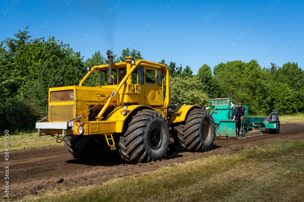 Closeup of a yellow tractor with heavy wheels in a field pulling a weight Closeup of a yellow tractor with heavy wheels in a field pulling a weight
