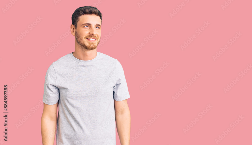 Handsome young man with bear wearing casual tshirt looking away to side with smile on face, natural expression. laughing confident. Handsome young man with bear wearing casual tshirt looking away to side with smile on face, natural expression. laughing confident.