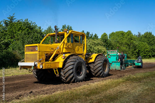 Closeup of a yellow tractor with heavy wheels in a field pulling a weight