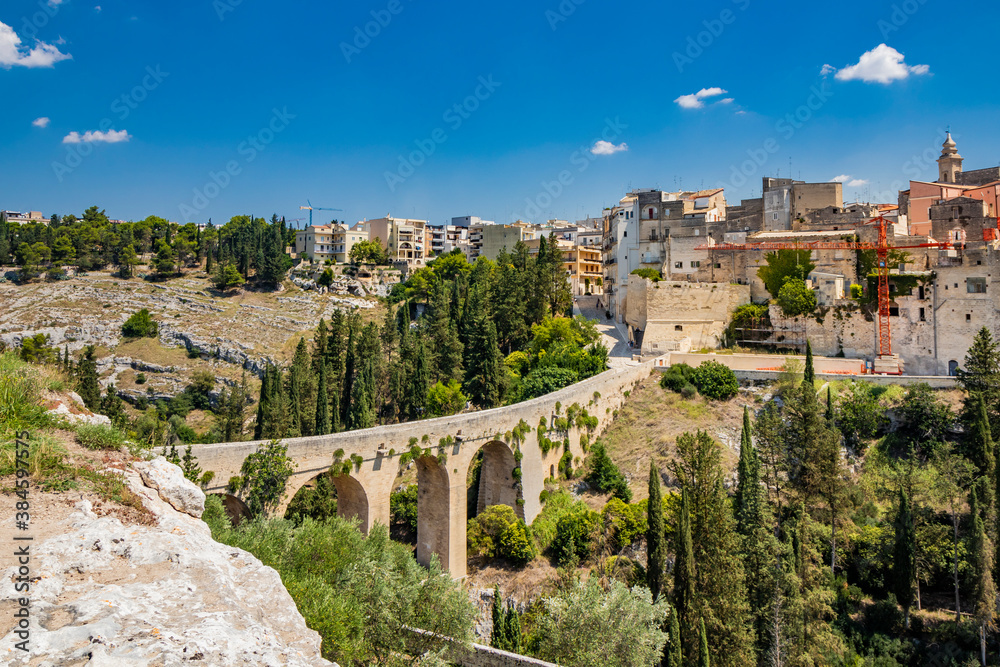 Gravina in Puglia, Italy. The stone bridge, ancient aqueduct and viaduct. On the other side of the valley where the Gravina stream flows, the skyline of the city with its houses and palaces.