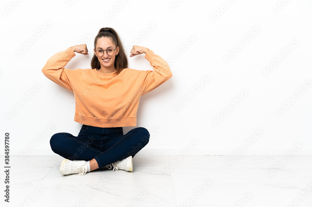 Young woman sitting on the floor doing strong gesture Young woman sitting on the floor doing strong gesture