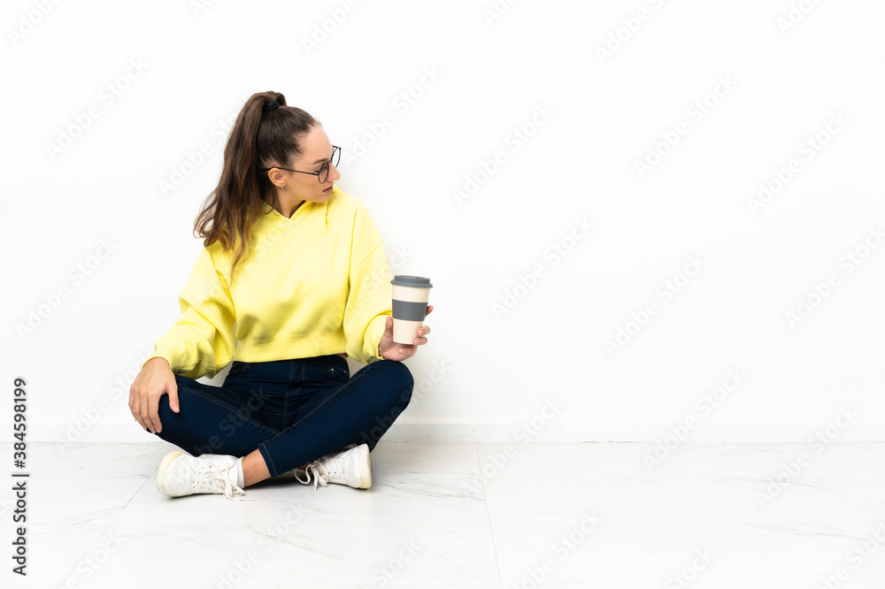 Young woman sitting on the floor holding a take away coffee in back position