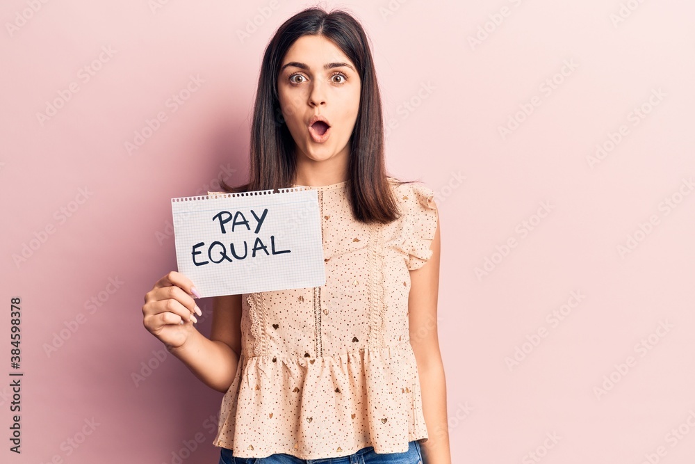 Young beautiful girl holding pay equal paper scared and amazed with open mouth for surprise, disbelief face Young beautiful girl holding pay equal paper scared and amazed with open mouth for surprise, disbelief face