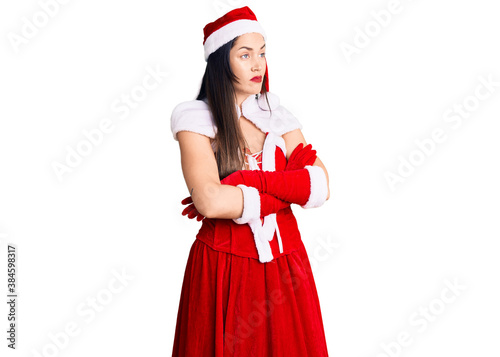 Young beautiful caucasian woman wearing santa claus costume looking to the side with arms crossed convinced and confident