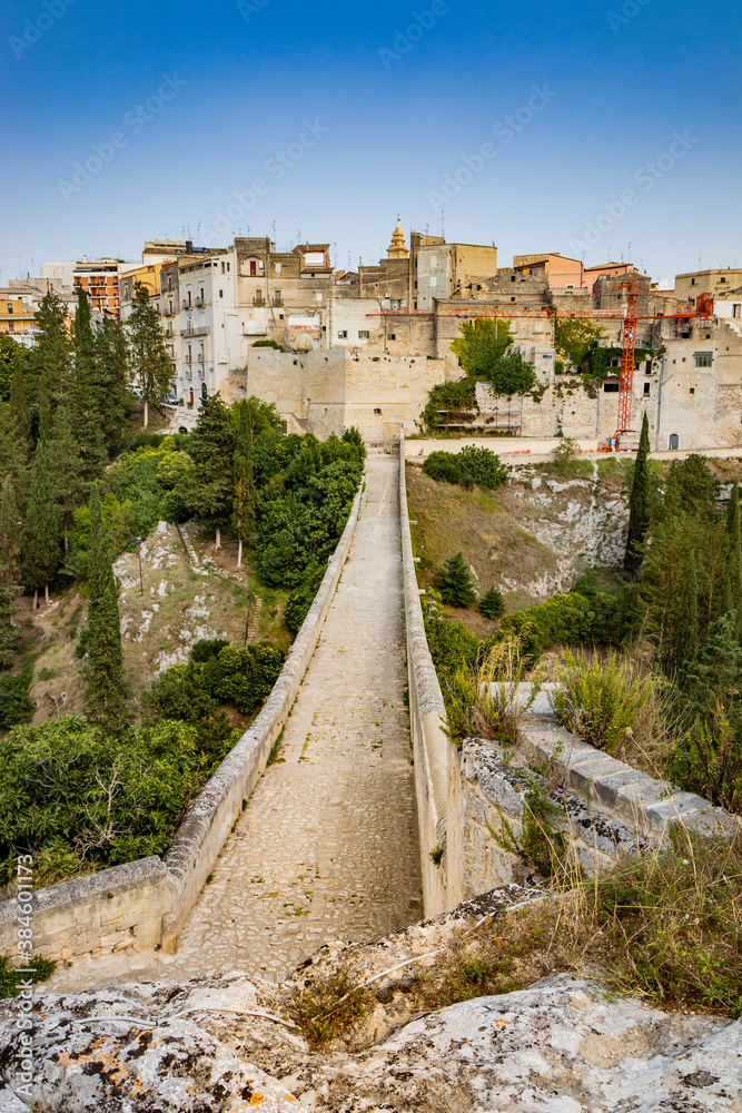 Gravina in Puglia, Italy. The stone bridge, ancient aqueduct and viaduct, over the Gravina stream. The Madonna della Stella Sanctuary, with its bell tower and the ancient cave church.