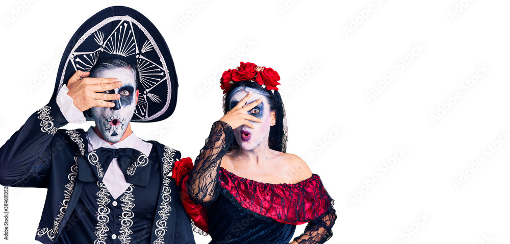 Young couple wearing mexican day of the dead costume over background peeking in shock covering face and eyes with hand, looking through fingers with embarrassed expression.