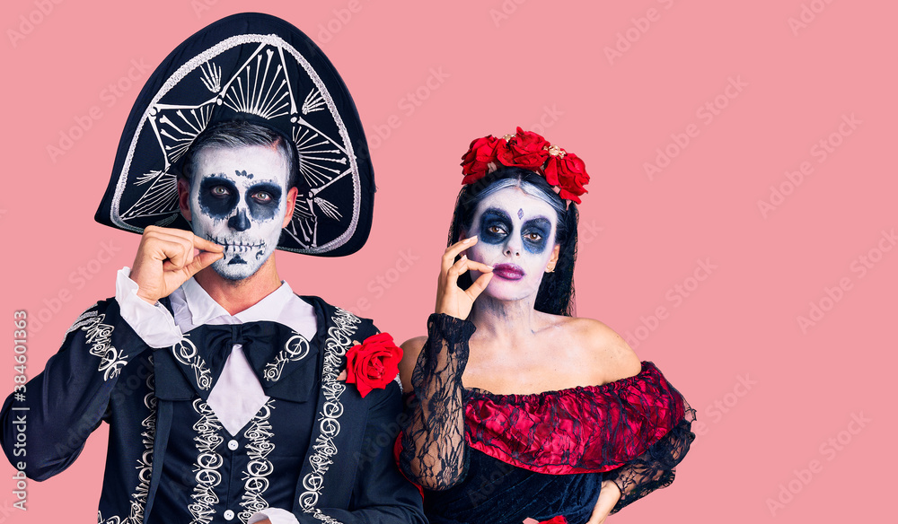 Young couple wearing mexican day of the dead costume over background mouth and lips shut as zip with fingers. secret and silent, taboo talking Young couple wearing mexican day of the dead costume over background mouth and lips shut as zip with fingers. secret and silent, taboo talking