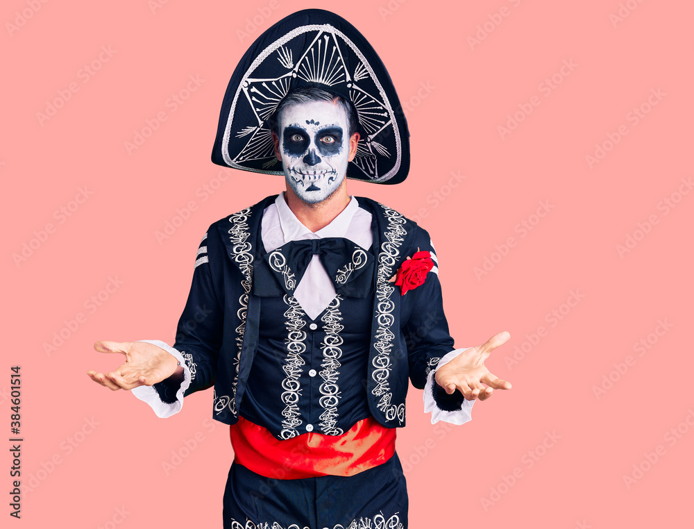 Young man wearing day of the dead costume over background clueless and confused expression with arms and hands raised. doubt concept. Young man wearing day of the dead costume over background clueless and confused expression with arms and hands raised. doubt concept.