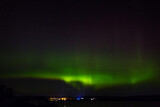 Aurora borealis over the city on the coast. Polar lights in the night starry sky over the lake.