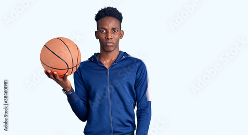 Young african american man holding basketball ball thinking attitude and sober expression looking self confident