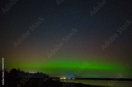 Aurora borealis over the city on the coast. Polar lights in the night starry sky over the lake.