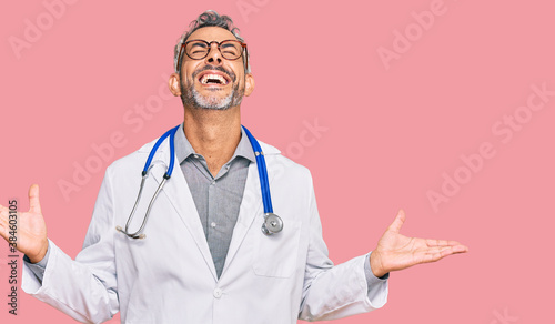 Middle age grey-haired man wearing doctor uniform and stethoscope celebrating mad and crazy for success with arms raised and closed eyes screaming excited. winner concept