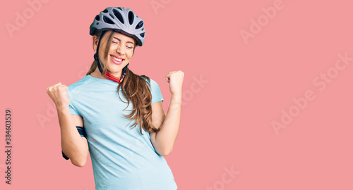 Beautiful caucasian young woman wearing bike helmet very happy and excited doing winner gesture with arms raised, smiling and screaming for success. celebration concept.