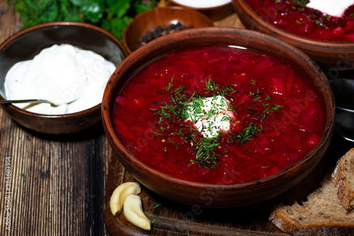 traditional russian dish borsch with sour cream and dill on wooden table, closeup