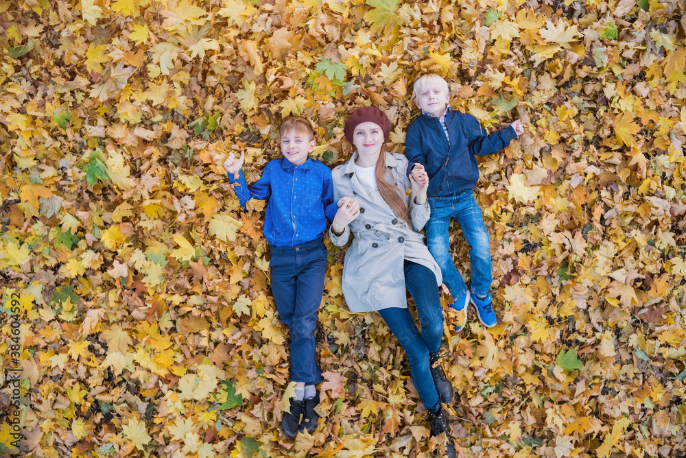 Happy family smiling while lying down in big pile of leaves. Mother and two sons in autumn Park. Top view. Happy family smiling while lying down in big pile of leaves. Mother and two sons in autumn Park. Top view.