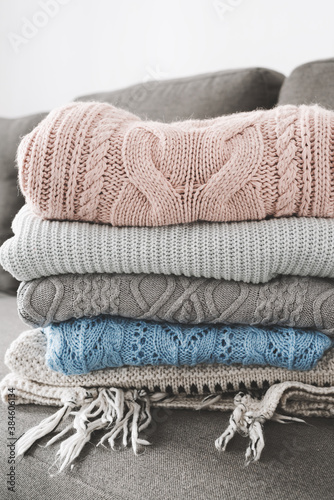 Pile of handmade knitted sweaters on gray sofa. Warm clothing. Knitwear care concept © VeronikaSmirnaya
