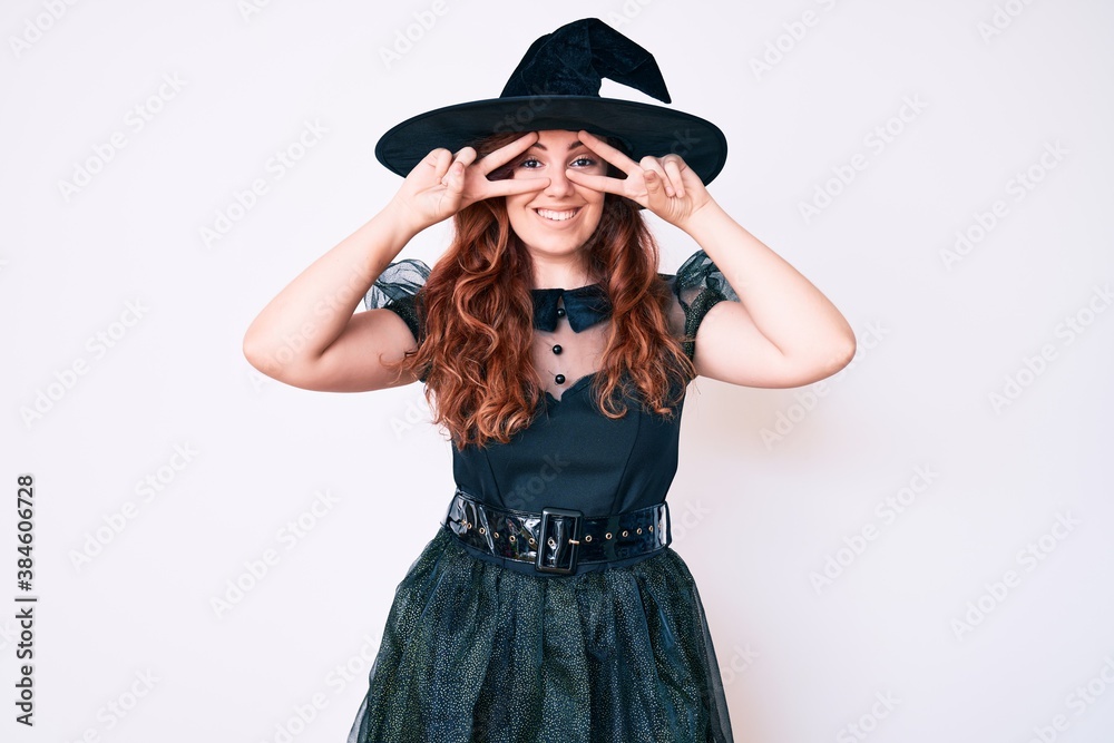 Young beautiful woman wearing witch halloween costume doing peace symbol with fingers over face, smiling cheerful showing victory Young beautiful woman wearing witch halloween costume doing peace symbol with fingers over face, smiling cheerful showing victory