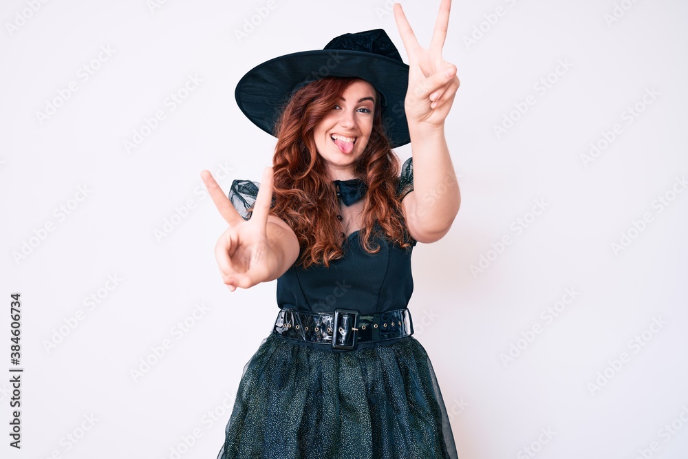 Young beautiful woman wearing witch halloween costume smiling with tongue out showing fingers of both hands doing victory sign. number two. Young beautiful woman wearing witch halloween costume smiling with tongue out showing fingers of both hands doing victory sign. number two.