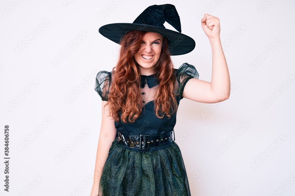 Young beautiful woman wearing witch halloween costume angry and mad raising fist frustrated and furious while shouting with anger. rage and aggressive concept. Young beautiful woman wearing witch halloween costume angry and mad raising fist frustrated and furious while shouting with anger. rage and aggressive concept.