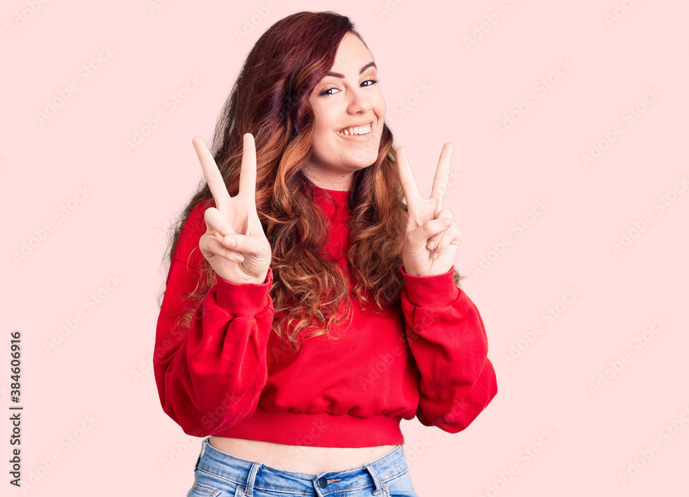 Young beautiful woman wearing casual winter sweater smiling looking to the camera showing fingers doing victory sign. number two.