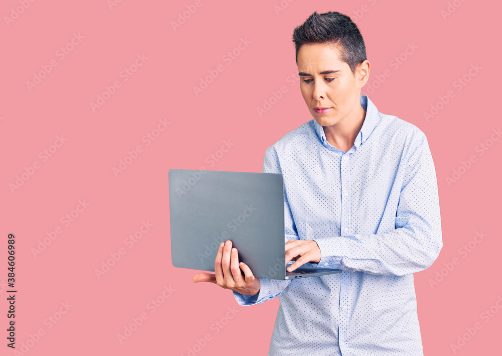 Young woman with short hair holding laptop thinking attitude and sober expression looking self confident Young woman with short hair holding laptop thinking attitude and sober expression looking self confident