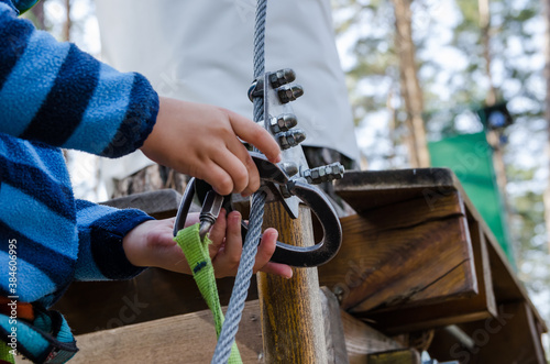 The boy climbs a rope park. Child's hands with safety harness.Close-up.