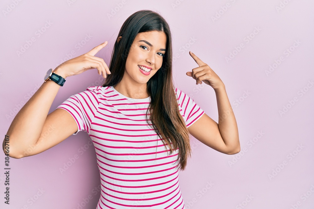 Young brunette woman wearing casual clothes over pink background smiling pointing to head with both hands finger, great idea or thought, good memory Young brunette woman wearing casual clothes over pink background smiling pointing to head with both hands finger, great idea or thought, good memory