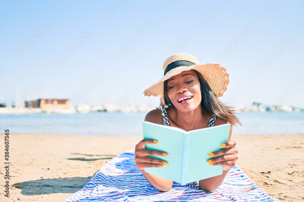 Young african american woman on vacation laying on the towel reading book at the beach