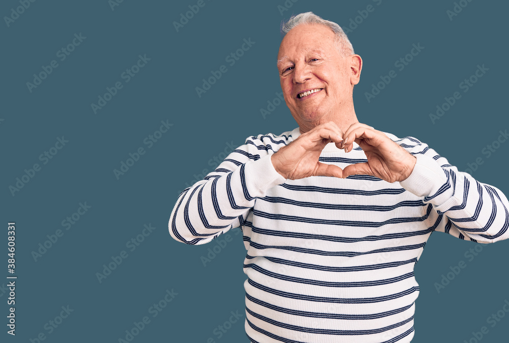 Senior handsome grey-haired man wearing casual striped sweater smiling in love showing heart symbol and shape with hands. romantic concept. Senior handsome grey-haired man wearing casual striped sweater smiling in love showing heart symbol and shape with hands. romantic concept.