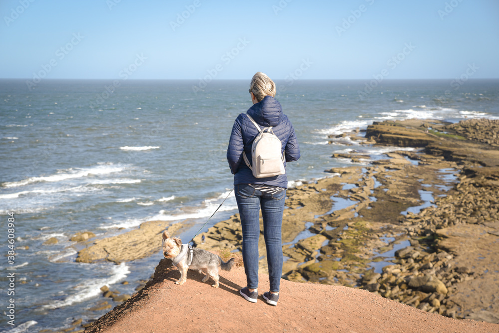 A woman with dog  looking off at sea  on peninsula cliff s edge in Finley UK