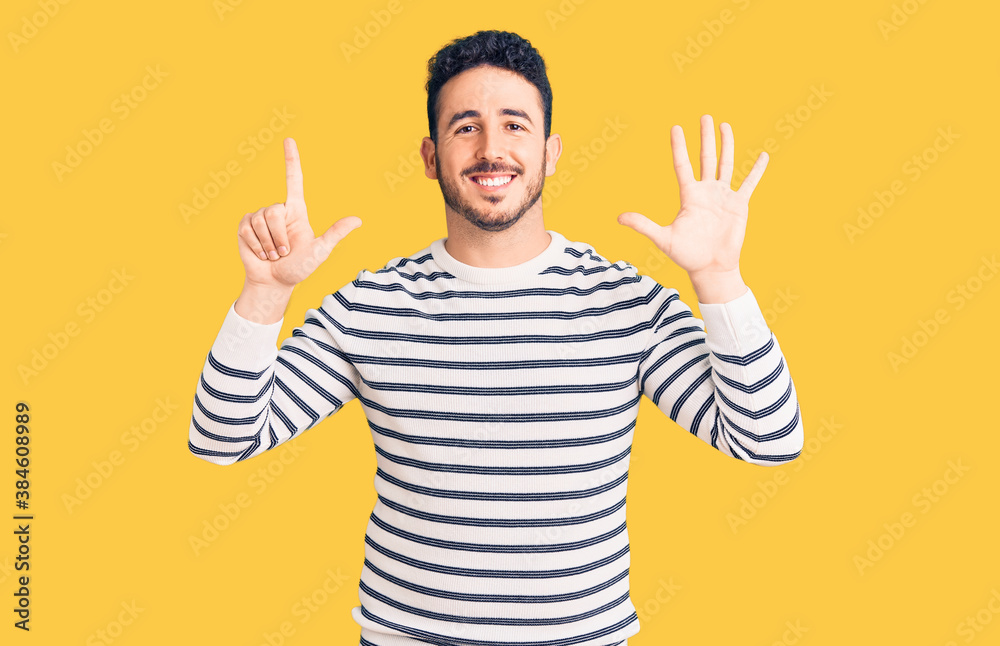 Naklejka premium Young hispanic man wearing casual clothes showing and pointing up with fingers number seven while smiling confident and happy.