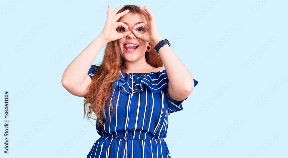 Young beautiful redhead woman wearing casual clothes doing ok gesture like binoculars sticking tongue out, eyes looking through fingers. crazy expression. Young beautiful redhead woman wearing casual clothes doing ok gesture like binoculars sticking tongue out, eyes looking through fingers. crazy expression.