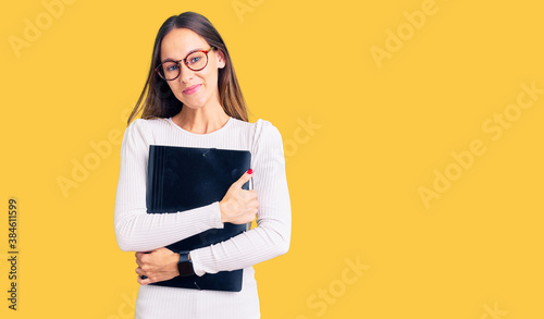 Beautiful brunette young woman holding business folder looking positive and happy standing and smiling with a confident smile showing teeth