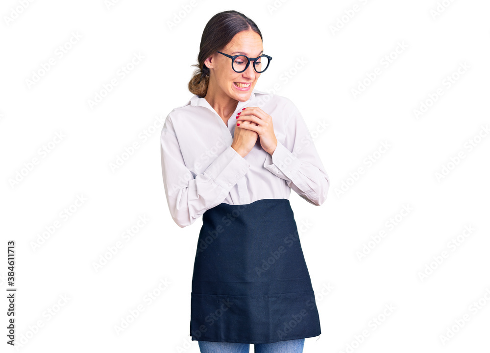 Beautiful brunette young woman wearing professional waitress apron laughing nervous and excited with hands on chin looking to the side Beautiful brunette young woman wearing professional waitress apron laughing nervous and excited with hands on chin looking to the side