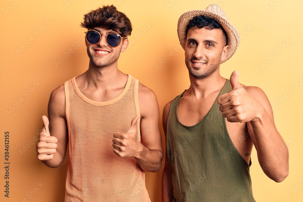 Naklejka premium Young gay couple wearing summer clothes success sign doing positive gesture with hand, thumbs up smiling and happy. cheerful expression and winner gesture.