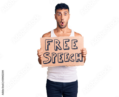 Young hispanic man holding free speech banner scared and amazed with open mouth for surprise, disbelief face