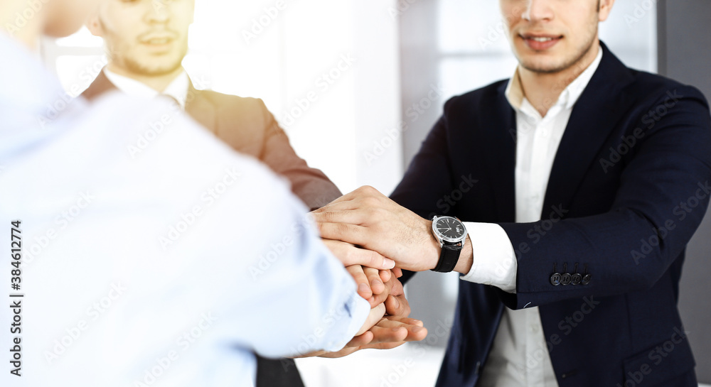 Business people group showing teamwork, joining hands and giving five to each other in sunny office