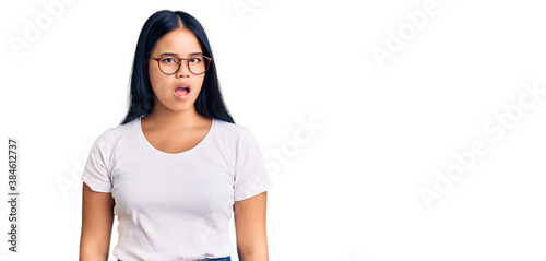 Young beautiful asian girl wearing casual clothes and glasses in shock face, looking skeptical and sarcastic, surprised with open mouth