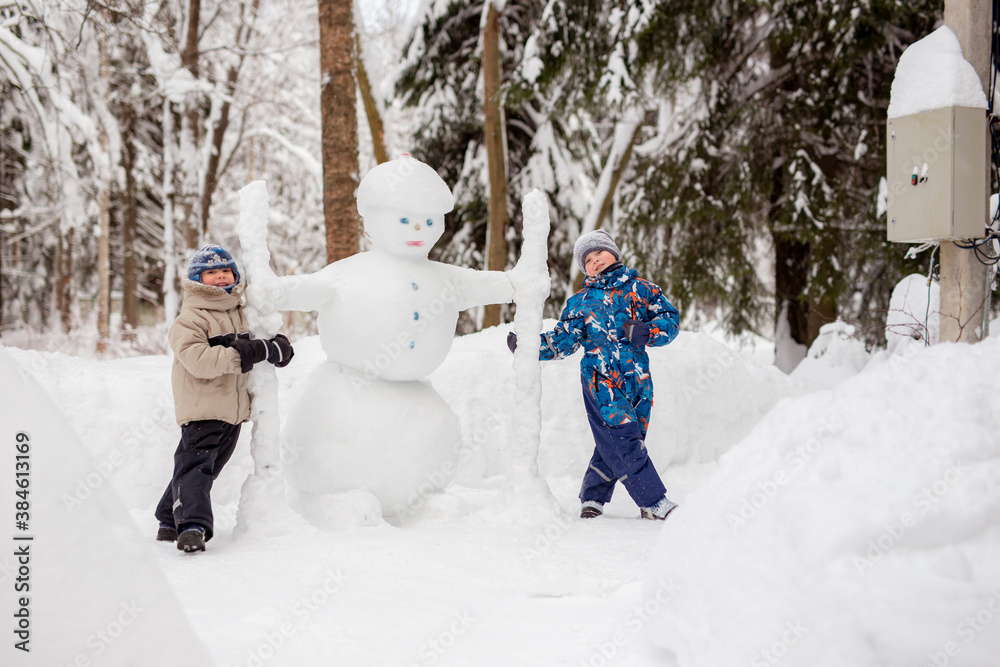 cute caucasian boys posing next to self made snowman in the countryside on winter day