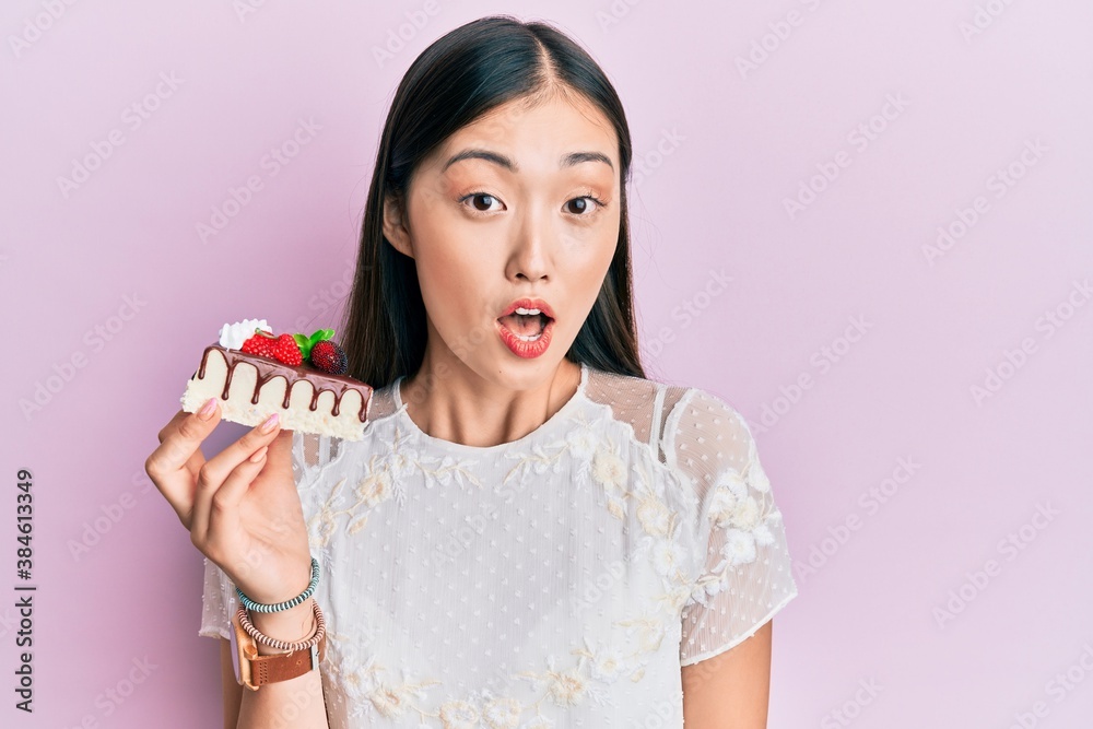 Young chinese woman eating a tasty cake scared and amazed with open mouth for surprise, disbelief face Young chinese woman eating a tasty cake scared and amazed with open mouth for surprise, disbelief face