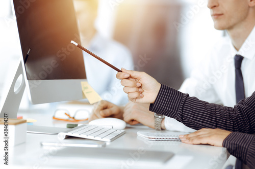 Business woman and man discussing questions while using computer and blocknote in sunny office, close-up photo