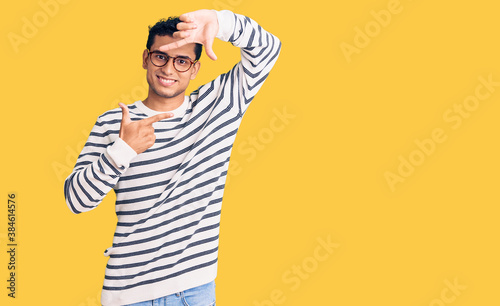 Hispanic handsome young man wearing casual clothes and glasses smiling making frame with hands and fingers with happy face. creativity and photography concept.