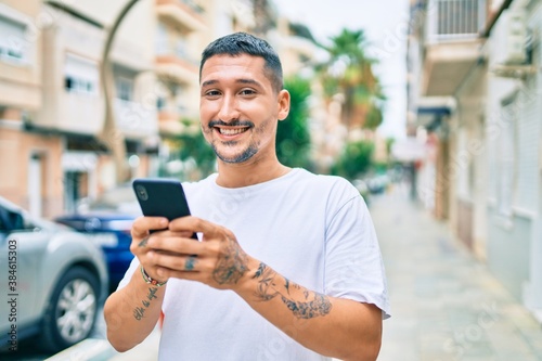 Young hispanic man smiling happy using smartphone at street of city.