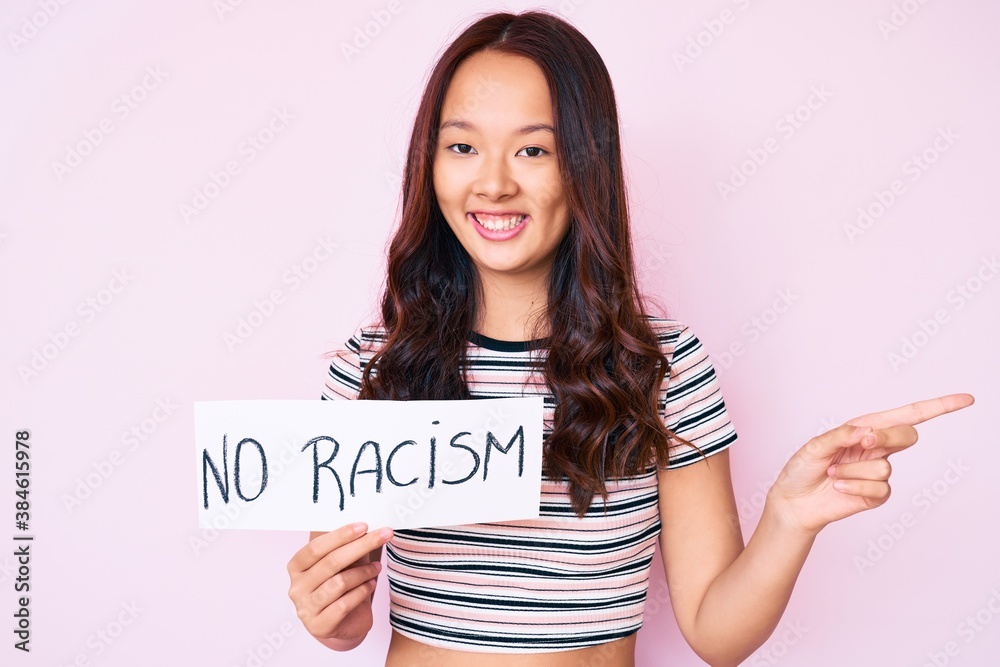 Young beautiful chinese girl holding no racism banner smiling happy pointing with hand and finger to the side Young beautiful chinese girl holding no racism banner smiling happy pointing with hand and finger to the side