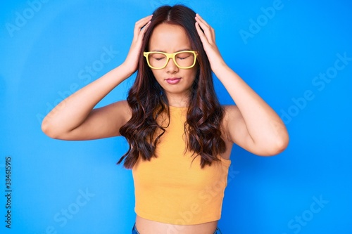 Young beautiful chinese girl wearing casual clothes and glasses suffering from headache desperate and stressed because pain and migraine. hands on head.