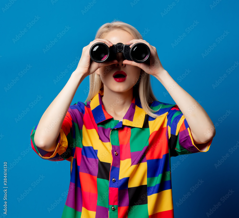 Blonde girl in 90s shirt with binoculars on blue background Blonde girl in 90s shirt with binoculars on blue background